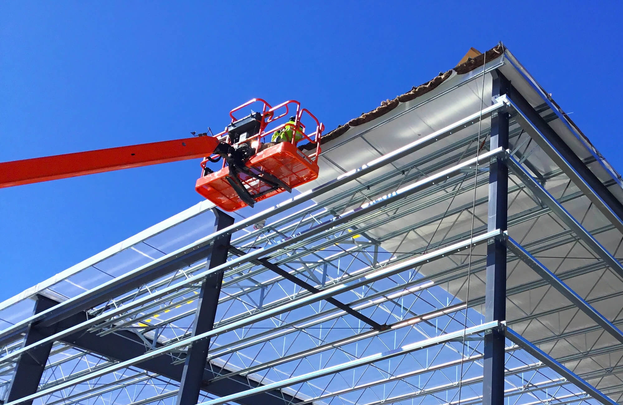 Sheridan Construction employee in a Boom lift, working on the installation of a metal roofing system.