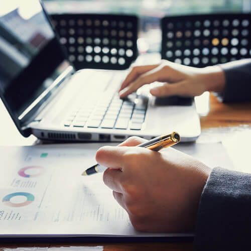 Person reviewing financial documents and working on a laptop.